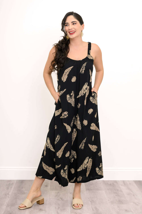 Woman smiling in a black jumpsuit with tan feather print, hands in pockets