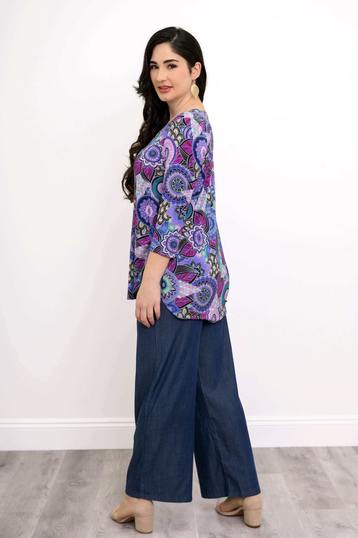 Side view of model wearing 3/4 sleeve purple patterned top, denim pants, and beige heels