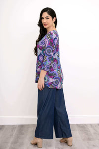 Side view of model wearing 3/4 sleeve purple patterned top, denim pants, and beige heels