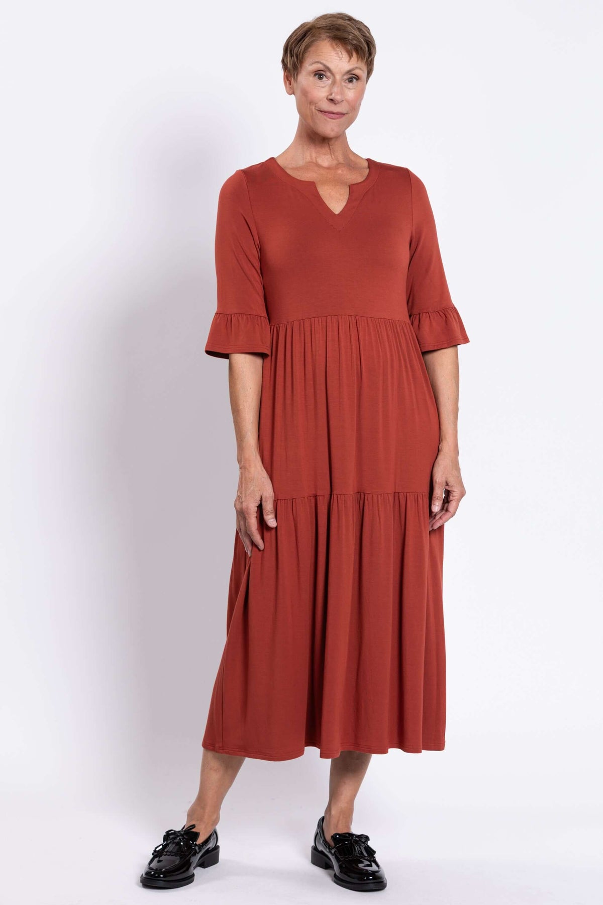 Model posing in rust-colored tiered midi dress with 3/4 ruffled sleeves