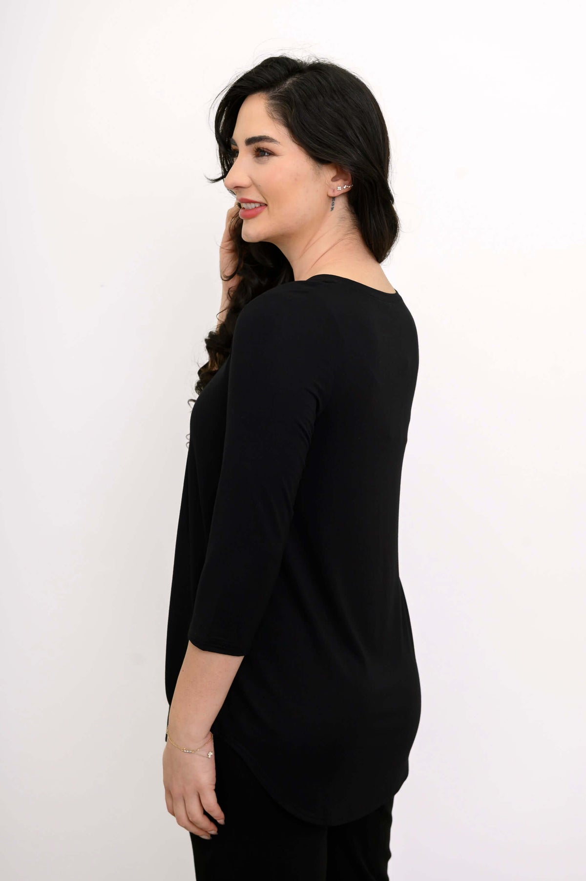Woman in a black 3/4 sleeve top, side view with hand near ear