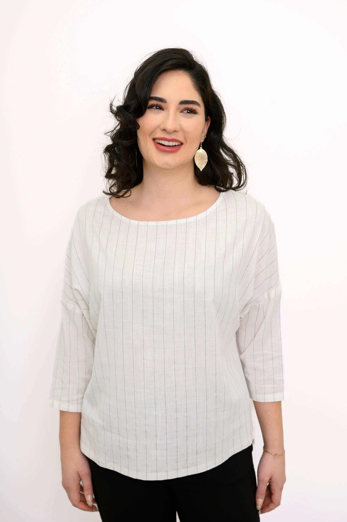 Close-up of woman wearing a white pinstripe top with 3/4 sleeves and gold leaf earrings