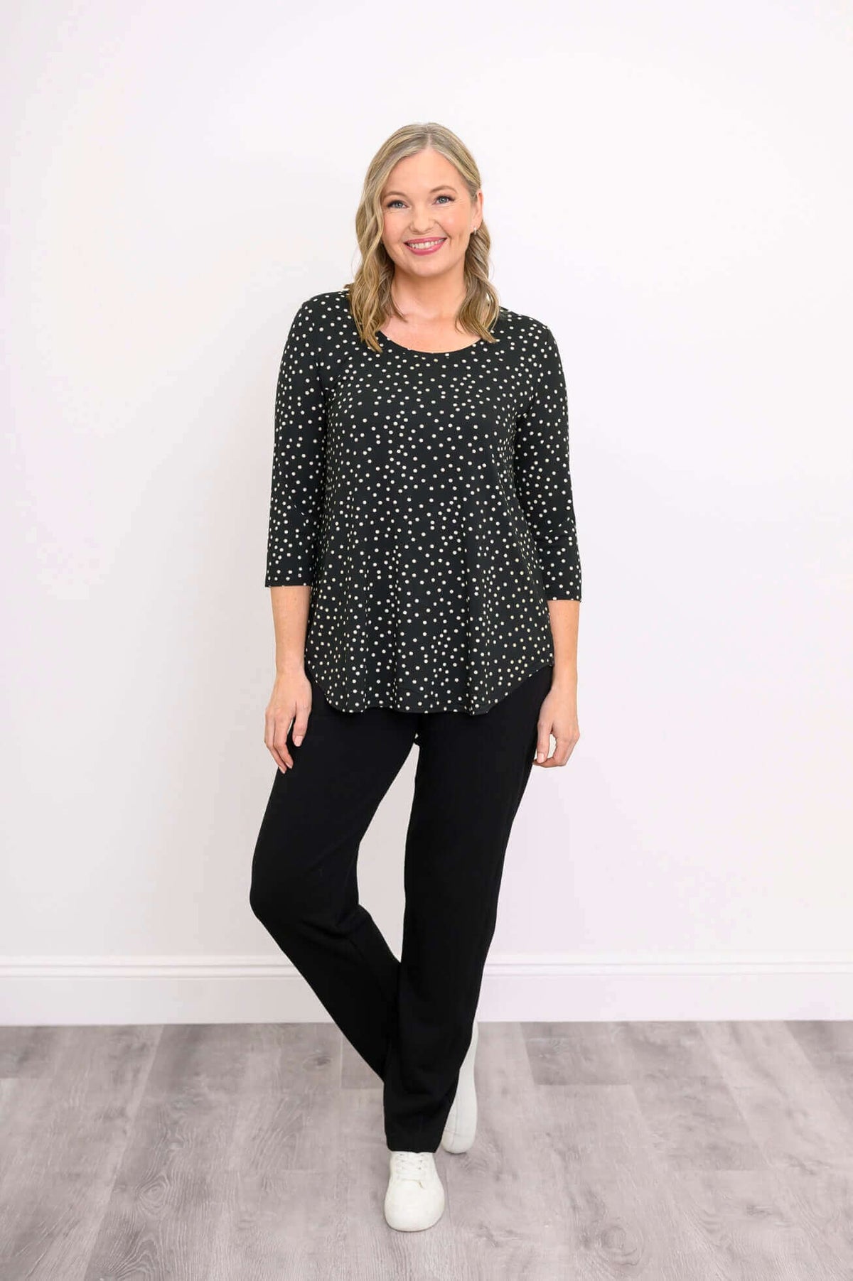 Woman in black polka dot 3/4 sleeve shirt, black pants, and white sneakers