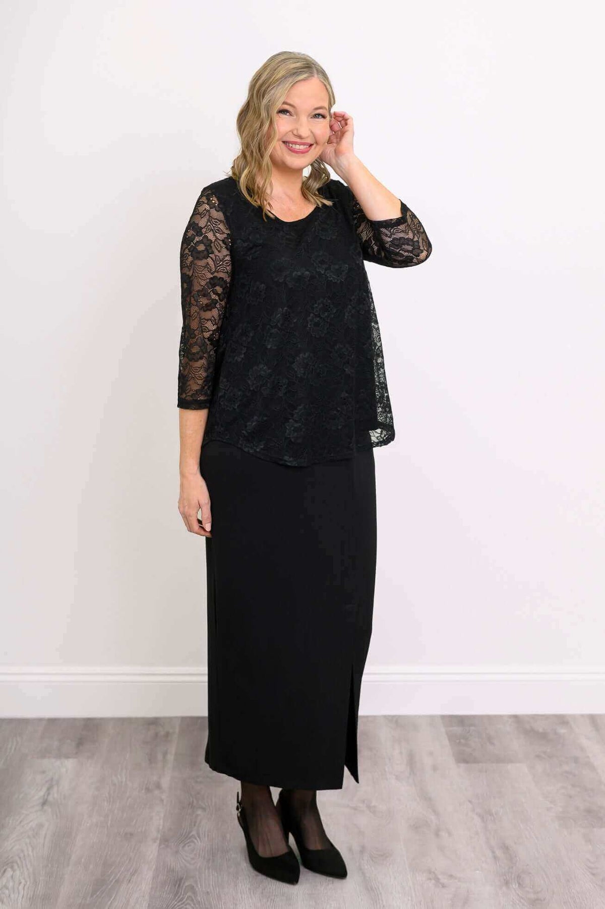 Woman posing in a black lace overlay top and long black skirt with 3/4 sleeves
