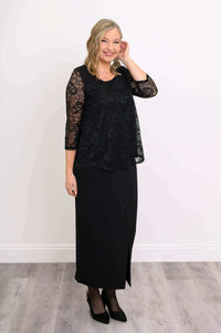 Woman posing in a black lace overlay top and long black skirt with 3/4 sleeves