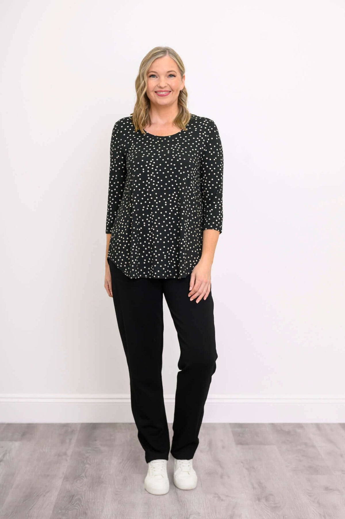 Woman in black polka dot 3/4 sleeve top and pants, hands at sides