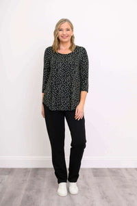 Woman in black polka dot 3/4 sleeve top and pants, hands at sides