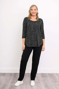 Smiling woman in black polka dot 3/4 sleeve top, black pants, and white sneakers