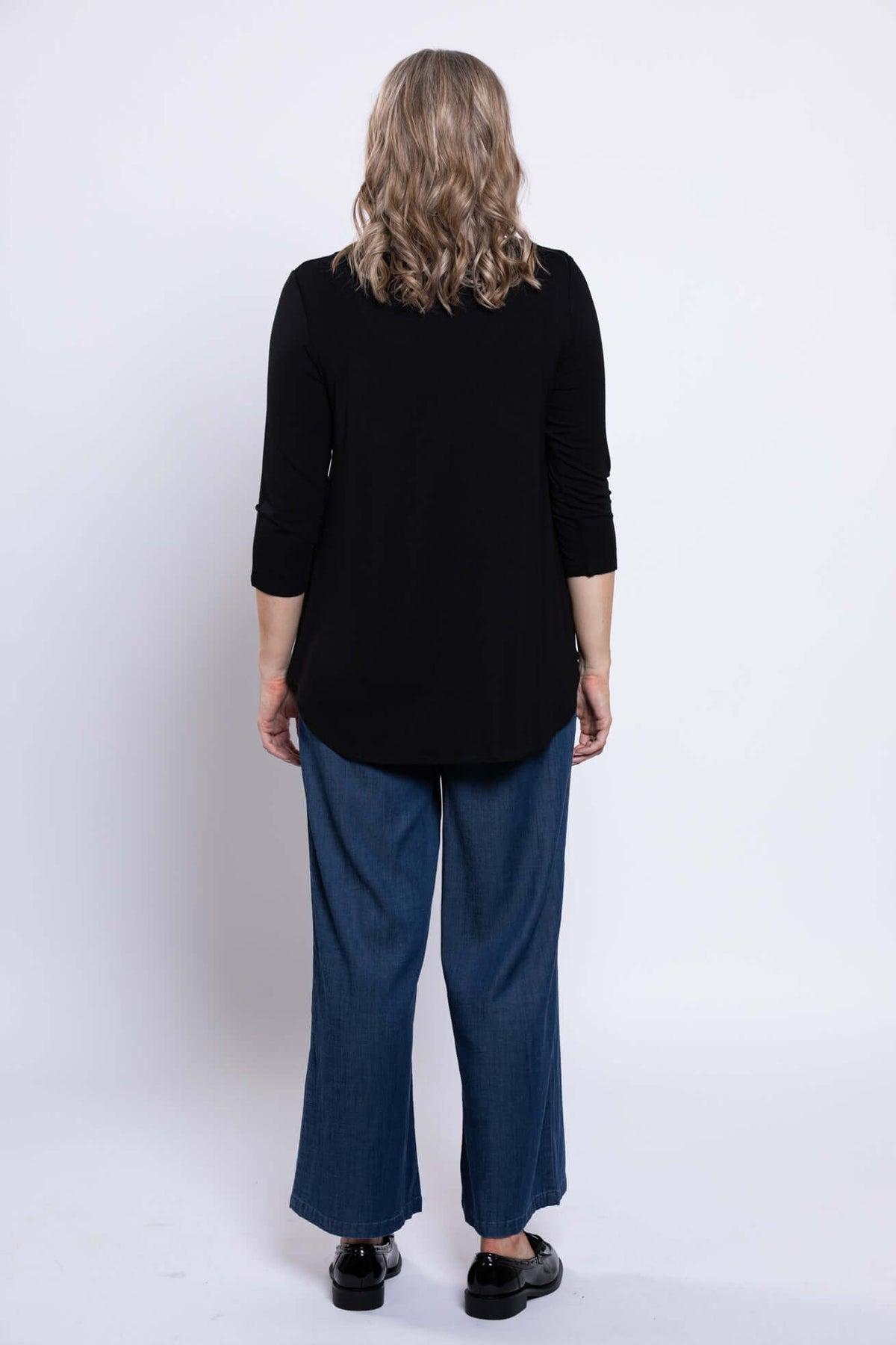 Woman wearing a black 3/4 sleeve top and blue jeans, back view