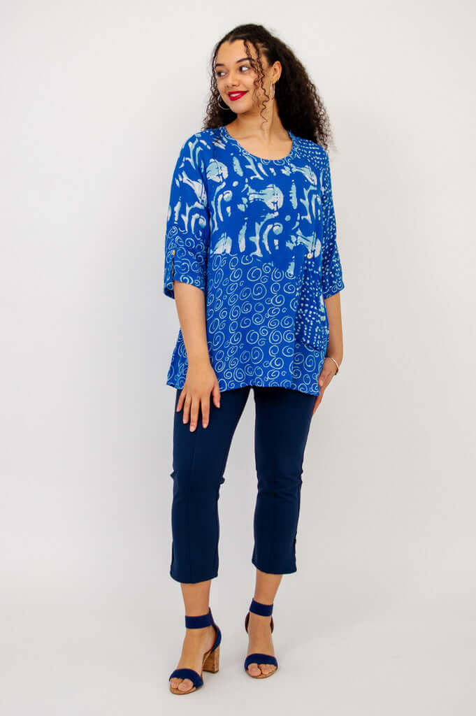 Woman posing sideways in a blue Palace Blouse with 3/4 sleeves, paired with navy pants and sandals