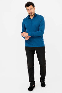 Man wearing a blue quarter-zip sweater and black pants, standing on white background