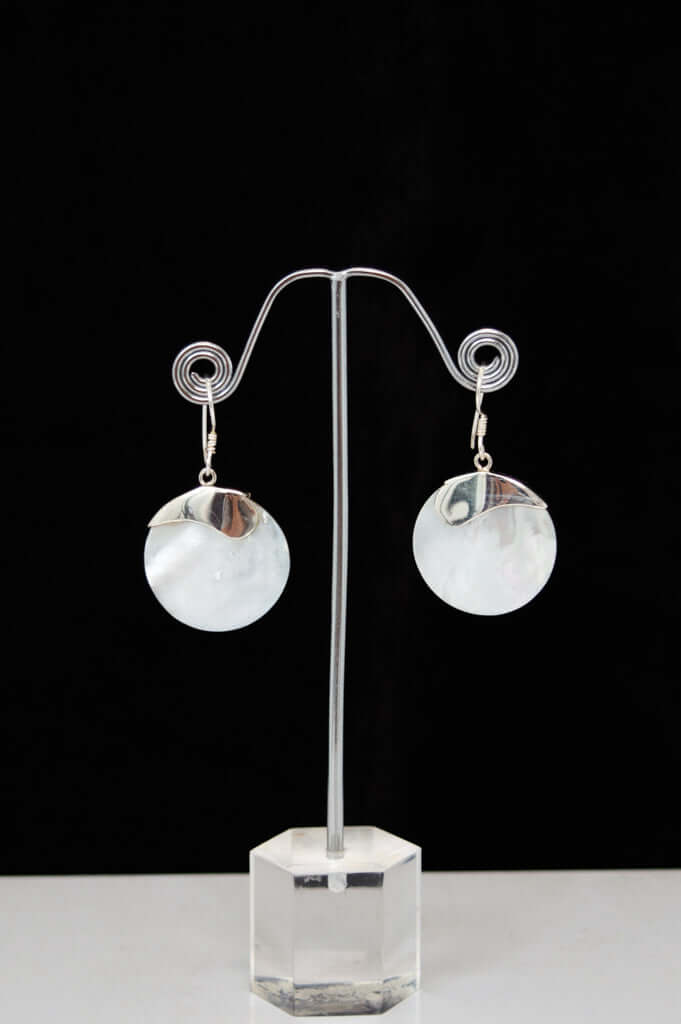 Pair of round mother-of-pearl and sterling silver earrings displayed on a stand