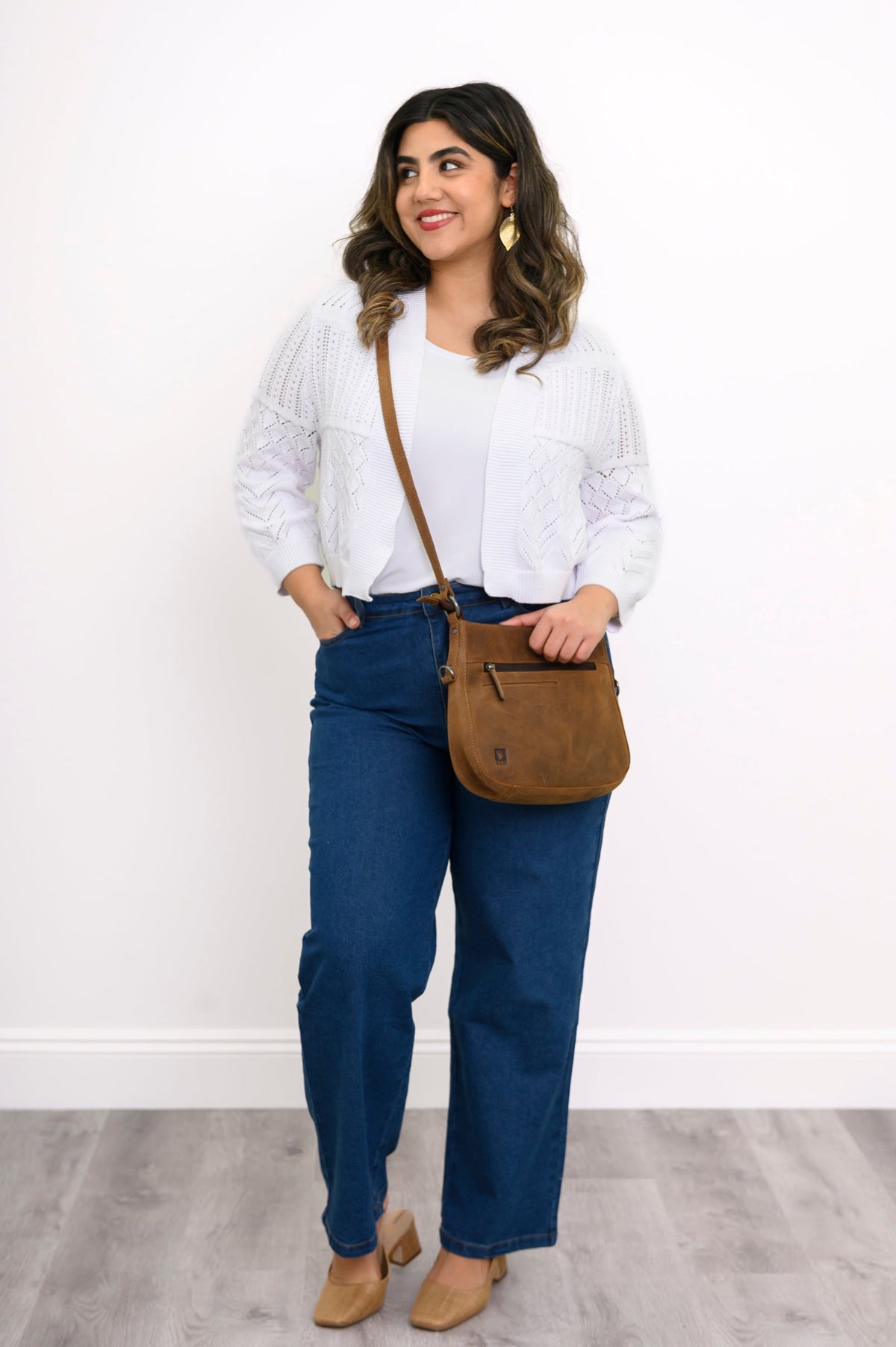 Woman wearing a white blouse, blue jeans, and brown shoes with a brown bag against a white background