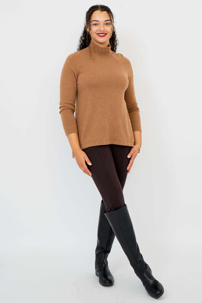 Woman in camel brown mock neck sweater and dark pants standing at an angle