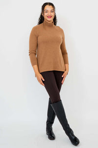 Woman in camel brown mock neck sweater and dark pants standing at an angle