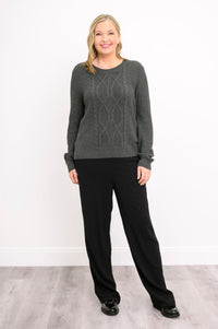 Front view of a female model wearing a graphite patterned sweater and black pants against a white wall and gray floor