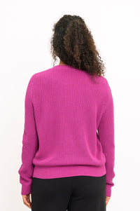 Back view of a female model wearing a textured magenta cotton-blend sweater and black pants, against a white backdrop