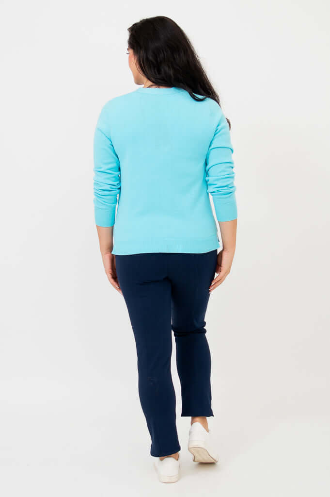 Back view of woman wearing aqua blue button-up cardigan, slim fit navy pants , and white sneakers