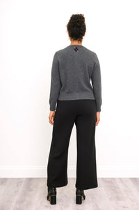 Back view of woman standing wearing a grey knit sweater with a small argyle emblem near the neck