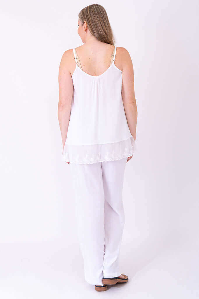 Back view of woman in white lace-trimmed tank top with adjustable straps and white pants
