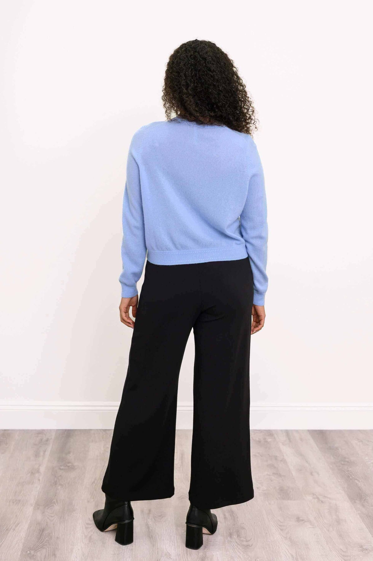 Back view of a woman wearing a blue cashmere cardigan and black pants