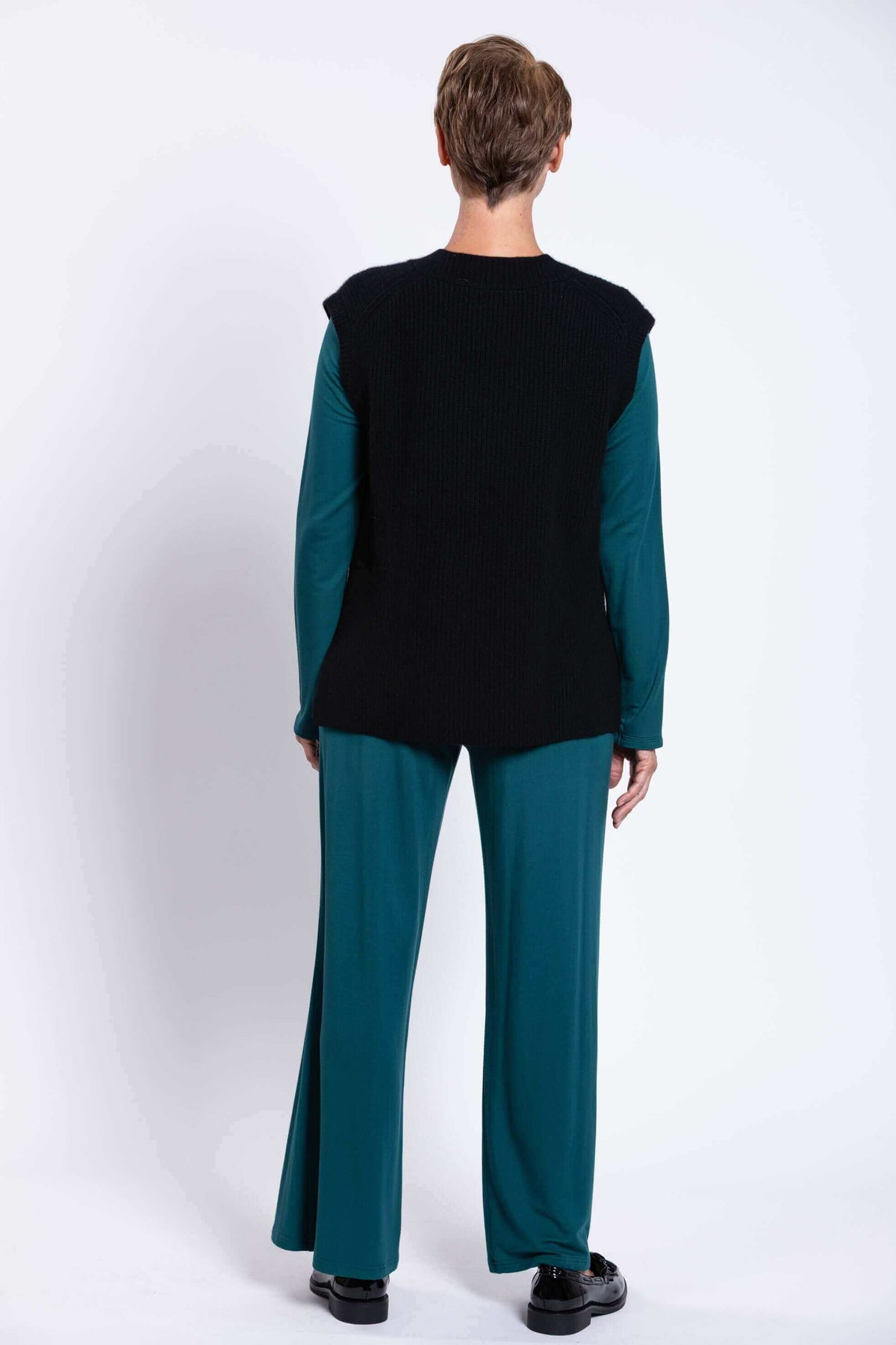 Back view of model wearing black ribbed knit vest over teal outfit