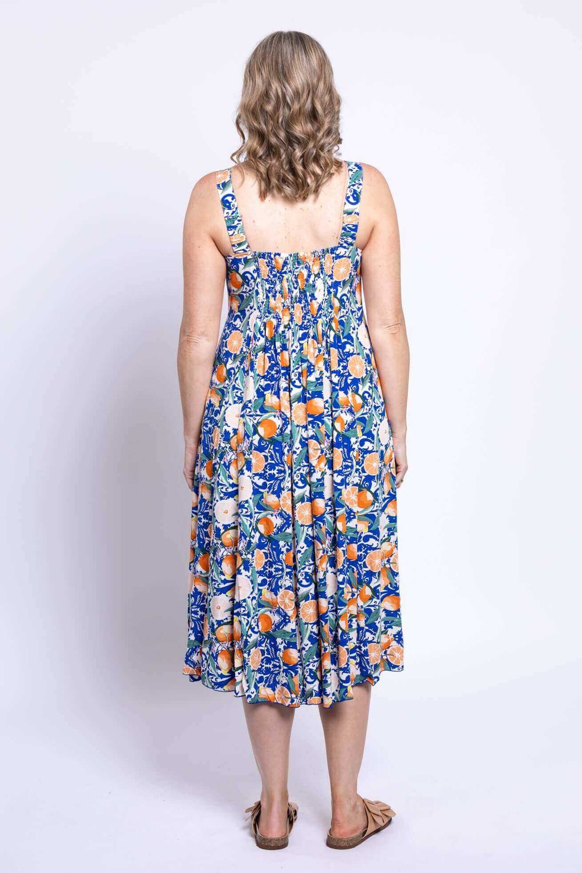 Back view of a woman wearing a sleeveless citrus floral dress with shirred bodice