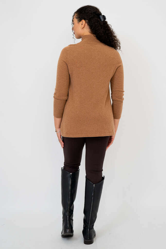 Back view of a woman wearing a camel brown mock neck sweater and dark pants