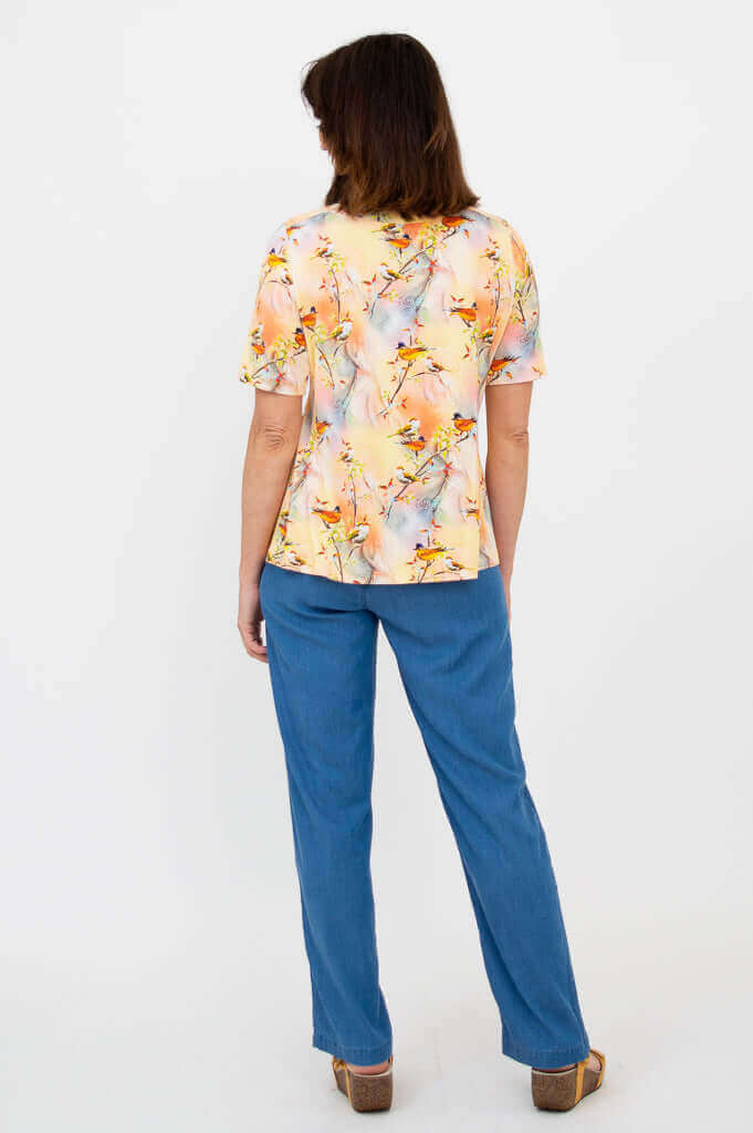 Back view of woman in a bird motif short sleeve tee and blue pants