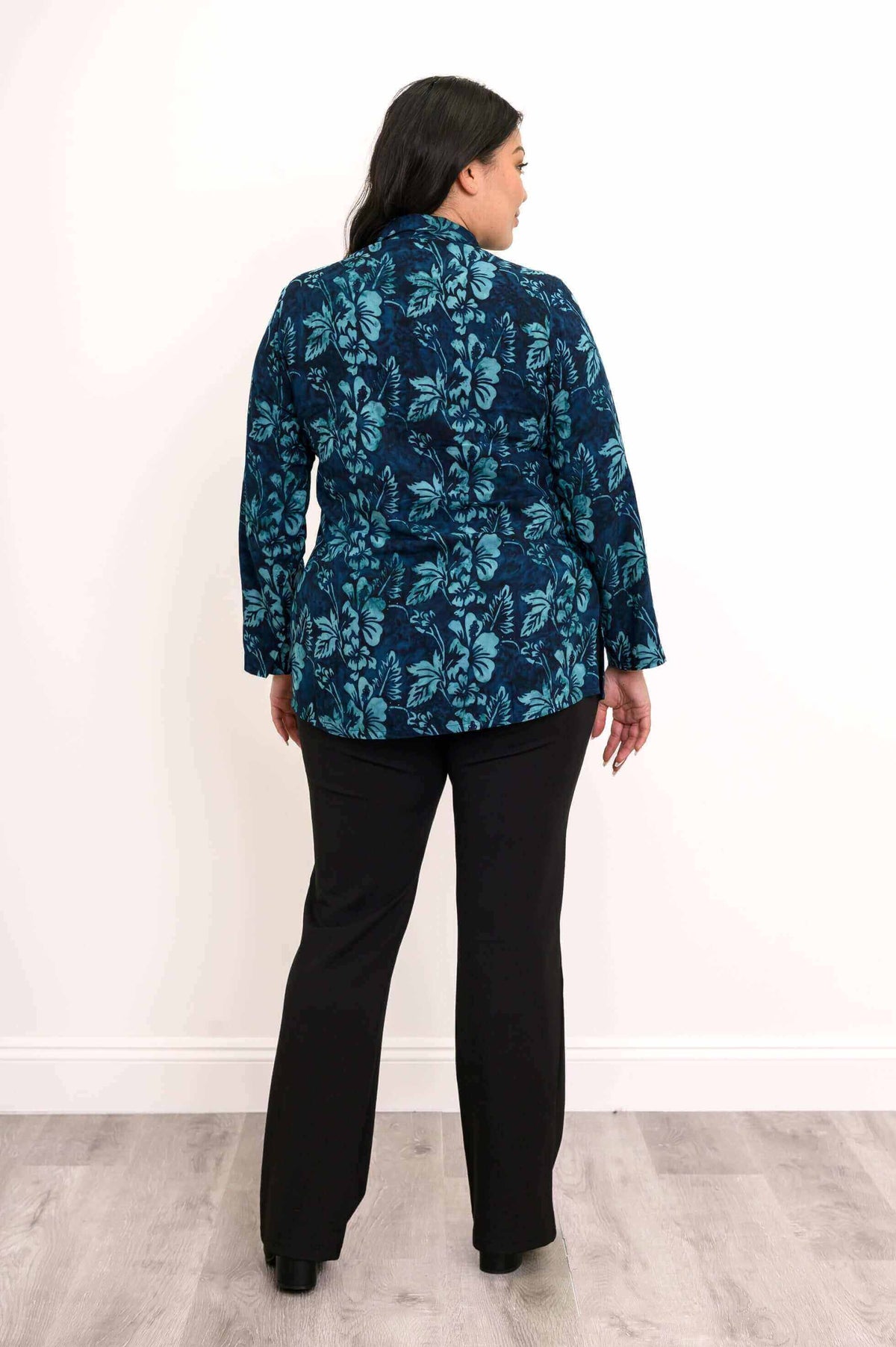 Back view of a blue floral blouse worn by a woman with long sleeves and black pants