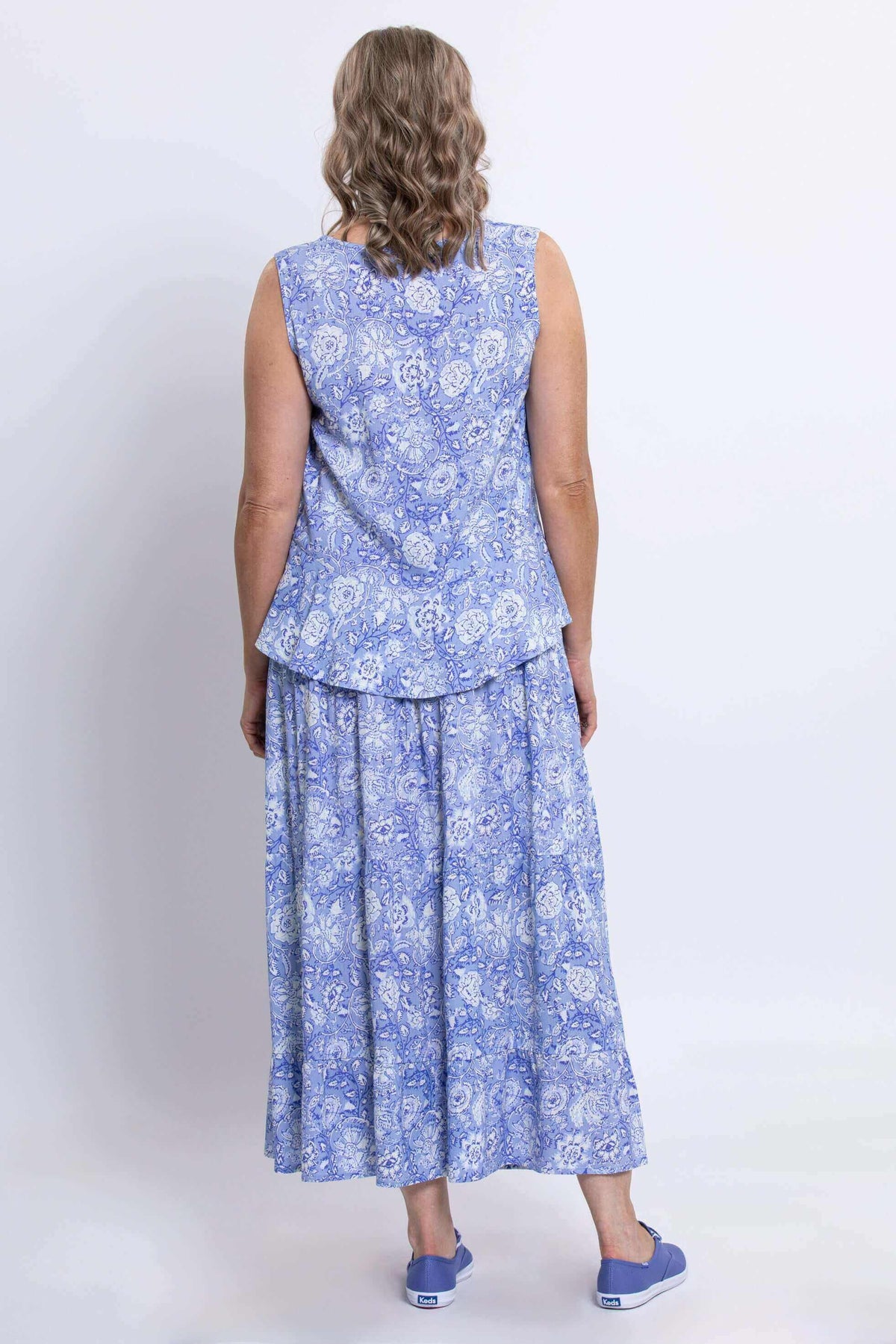 Full body back view of woman wearing a flowing light blue floral top and layered matching maxi skirt