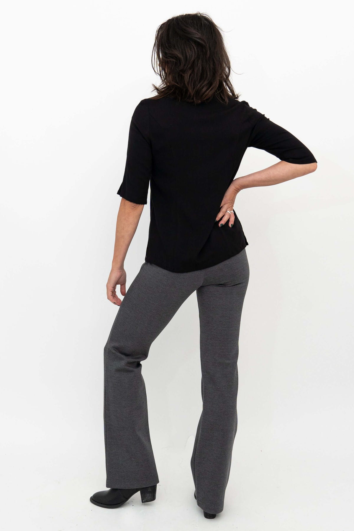 Woman modeling granite grey flare pants and black shirt, back view