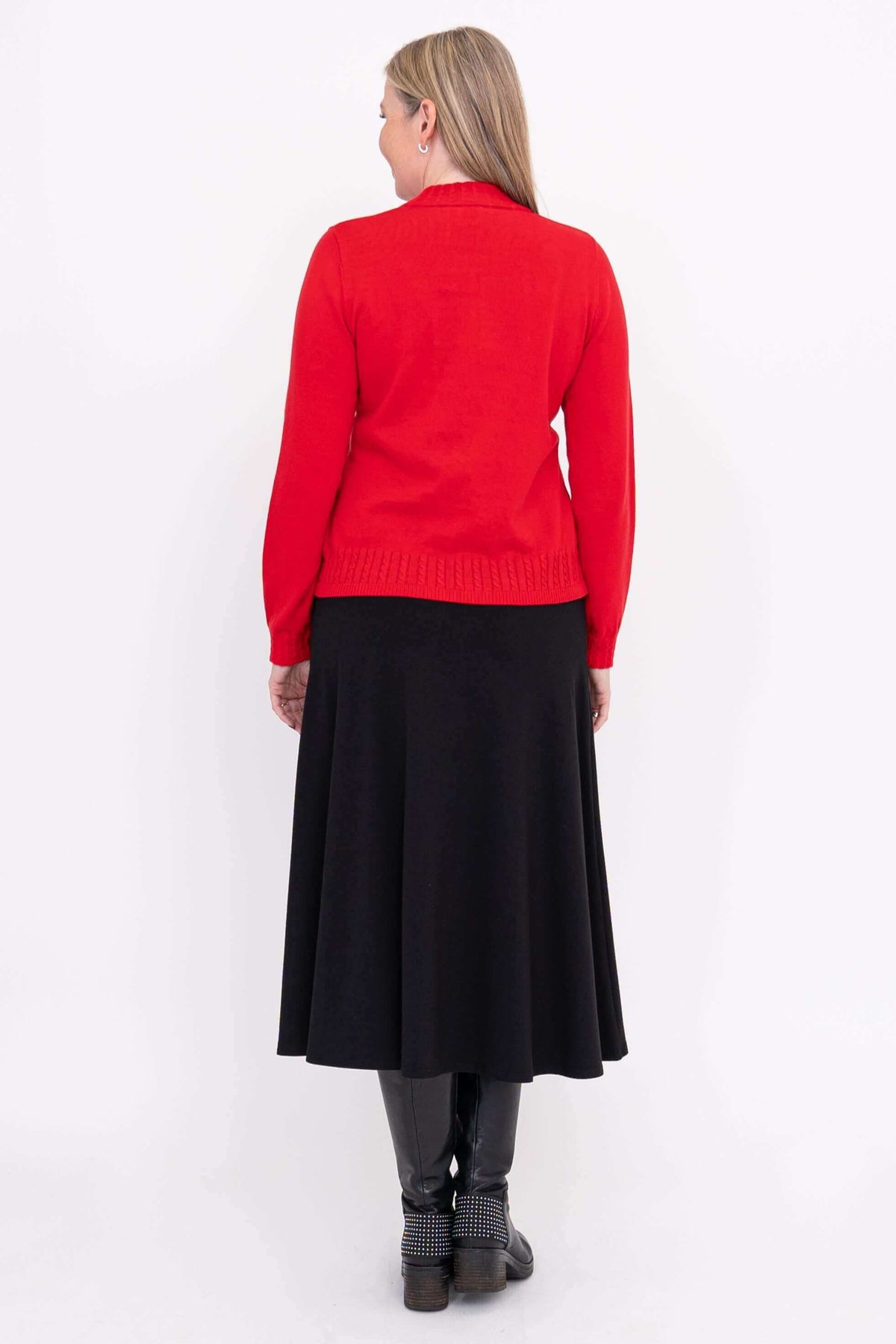 Back view of a woman wearing a red sweater and black skirt, showing cable knit hem