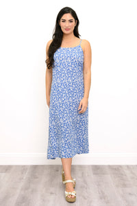 A woman modeling a sleeveless midi dress with a blue and white floral pattern, standing against a white wall on a light gray wood floor.