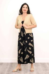 Woman wearing a beige cardigan over a black printed dress, holding the cardigan open