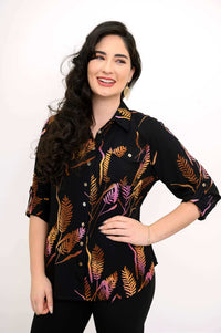 Woman wearing a black button-up shirt with orange and purple botanical print, smiling