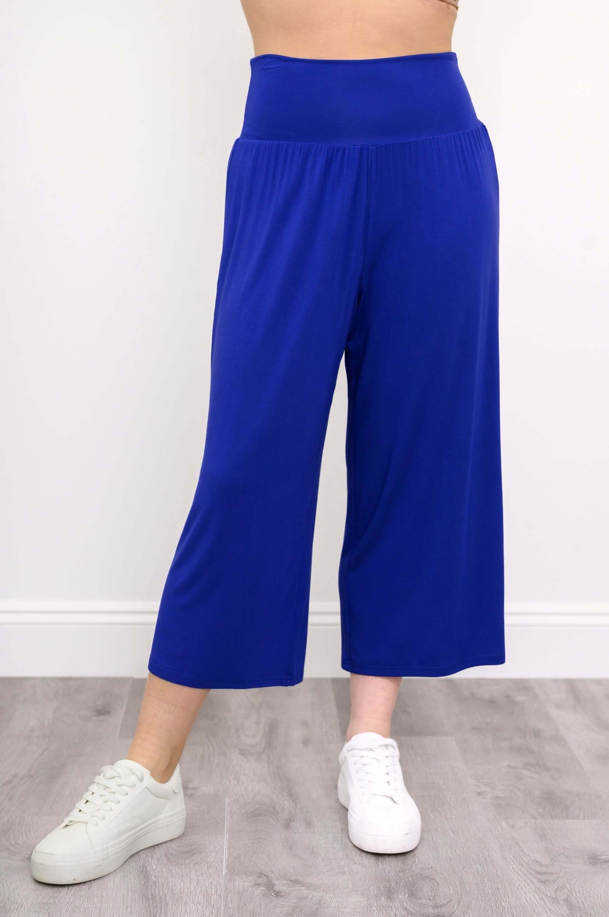 Blue cropped capri pants with wide waistband, front view with white sneakers