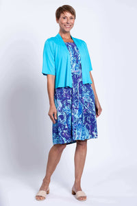 Woman in a sleeveless blue paisley dress styled with a turquoise open-front shrug