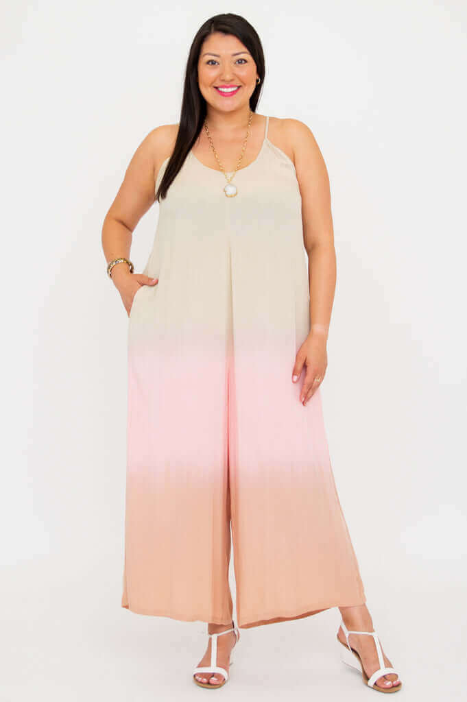 Woman wearing blush ombre wide-leg jumpsuit with spaghetti straps, posing against a white background