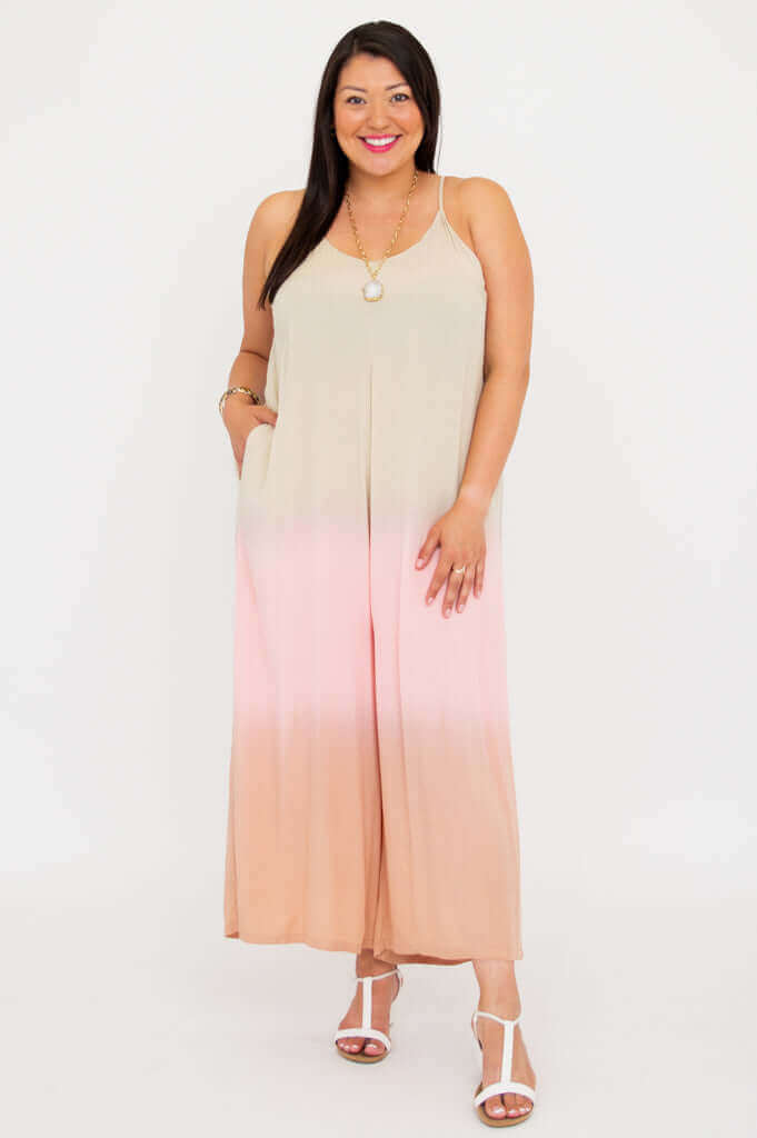 Front view of woman smiling in blush ombre jumpsuit with adjustable straps, white background