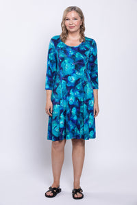 Full body view of woman wearing 3/4 sleeve short dress with bright blue print and sandals