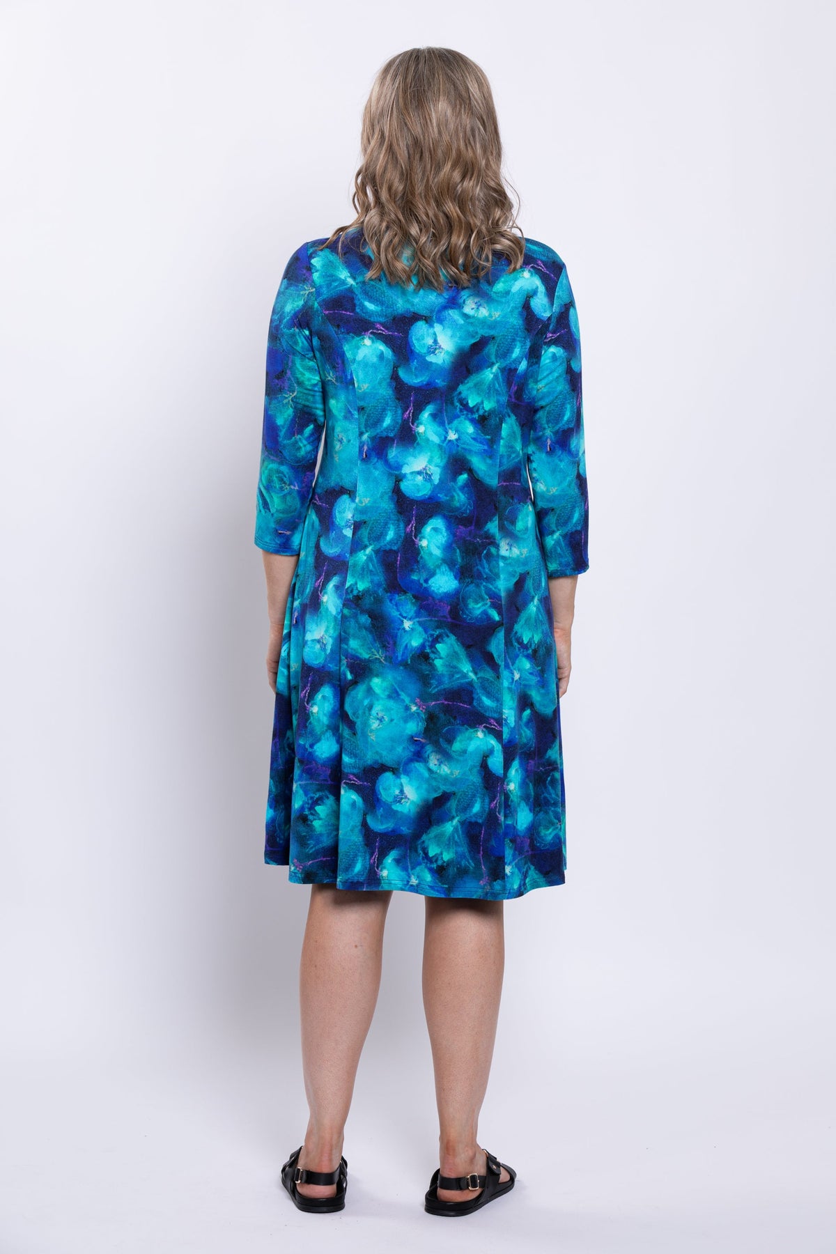 Rear view of woman wearing an ocean print blue knee-length dress against a white background