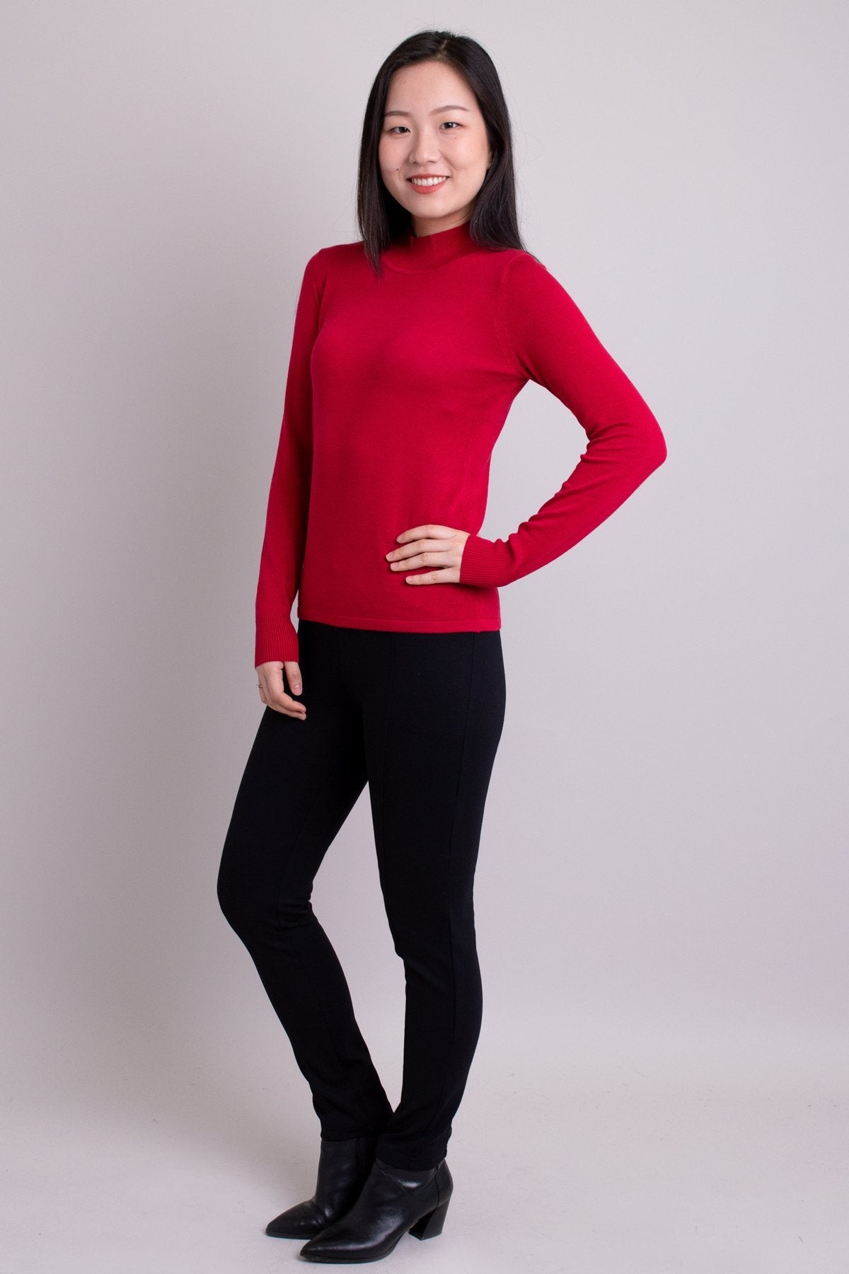 Women's red long-sleeve mock neck sweater worn with black pants. Made with sustainable and natural fibers, fair-trade.
