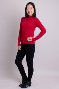 Women's red long-sleeve mock neck sweater worn with black pants. Made with sustainable and natural fibers, fair-trade.