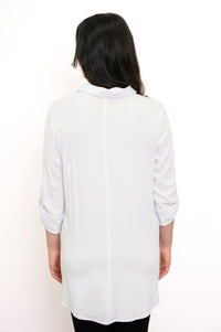 Back view of woman wearing a white tunic and black pants against a white background