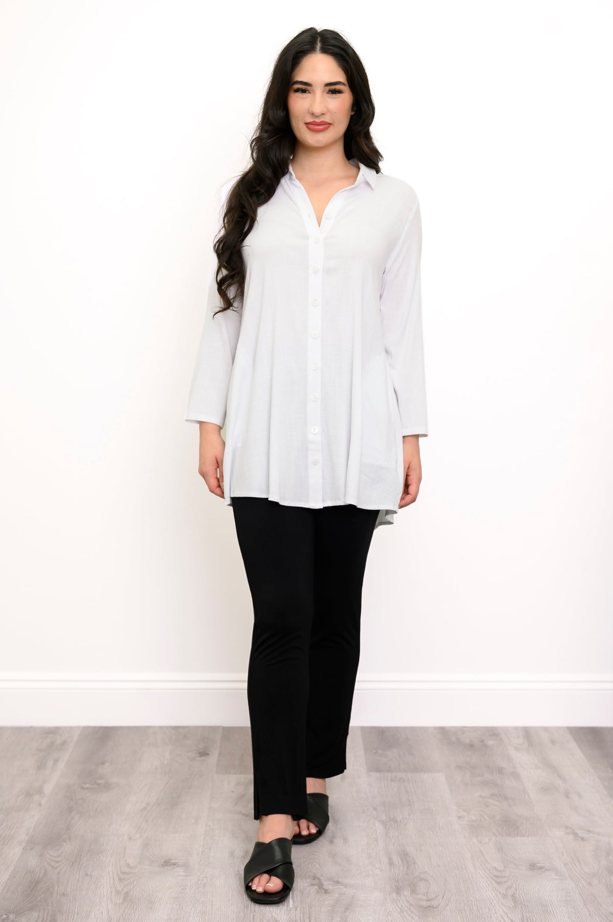 Full body view of woman wearing white button up blouse and black pants against a white background