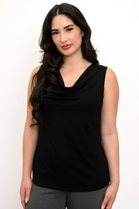 Close up view of woman smiling and wearing a black tank top and grey pants against a white background