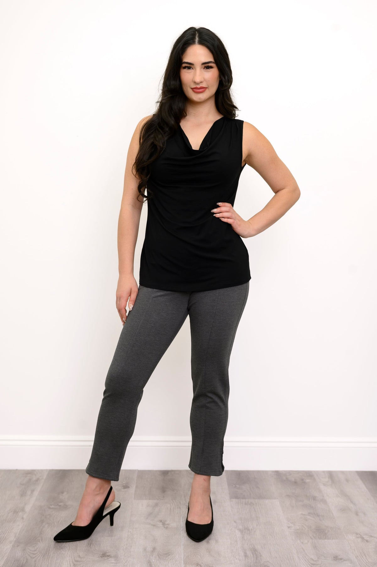 Woman posing with her hand on her hip while wearing a black sleeveless top and grey pants