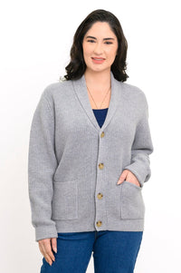 Woman wearing grey knit cardigan and denim pants on a white background, front view