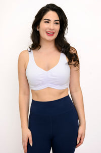 Woman wearing a white bralette and navy leggings on a white background, front view